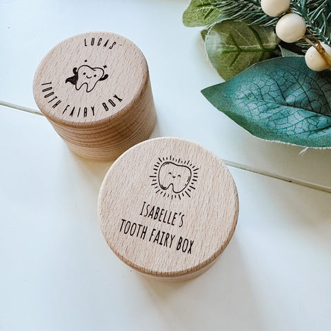 Two wooden tooth fairy boxes with personalized names on a light background with green leaves.